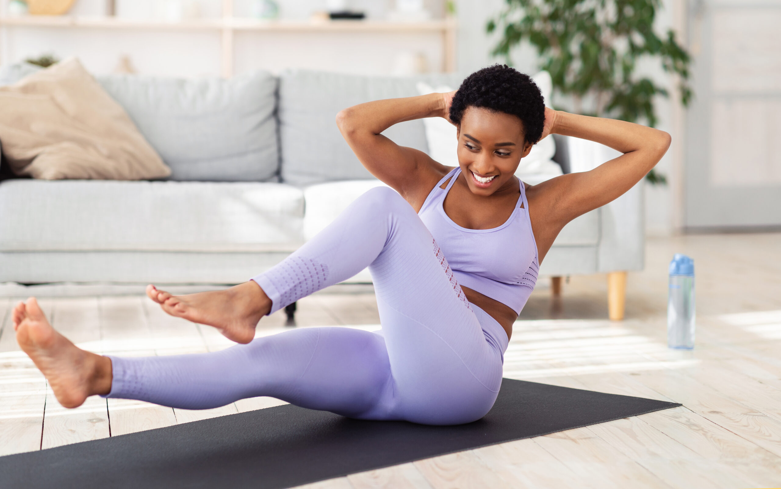Sports during lockdown. Beautiful black lady doing home fitness on yoga mat, working out her whole body. Lovely African American woman having domestic training, exercising in living room