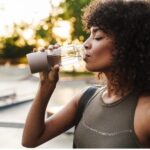 Young African American woman drinking water from a reusable bottle after a run 