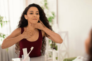 Beautiful young woman making lymphatic drainage neck self massage in front of mirror at bathroom, copy space. Pretty millennial lady doing domestic skin care procedure at home
